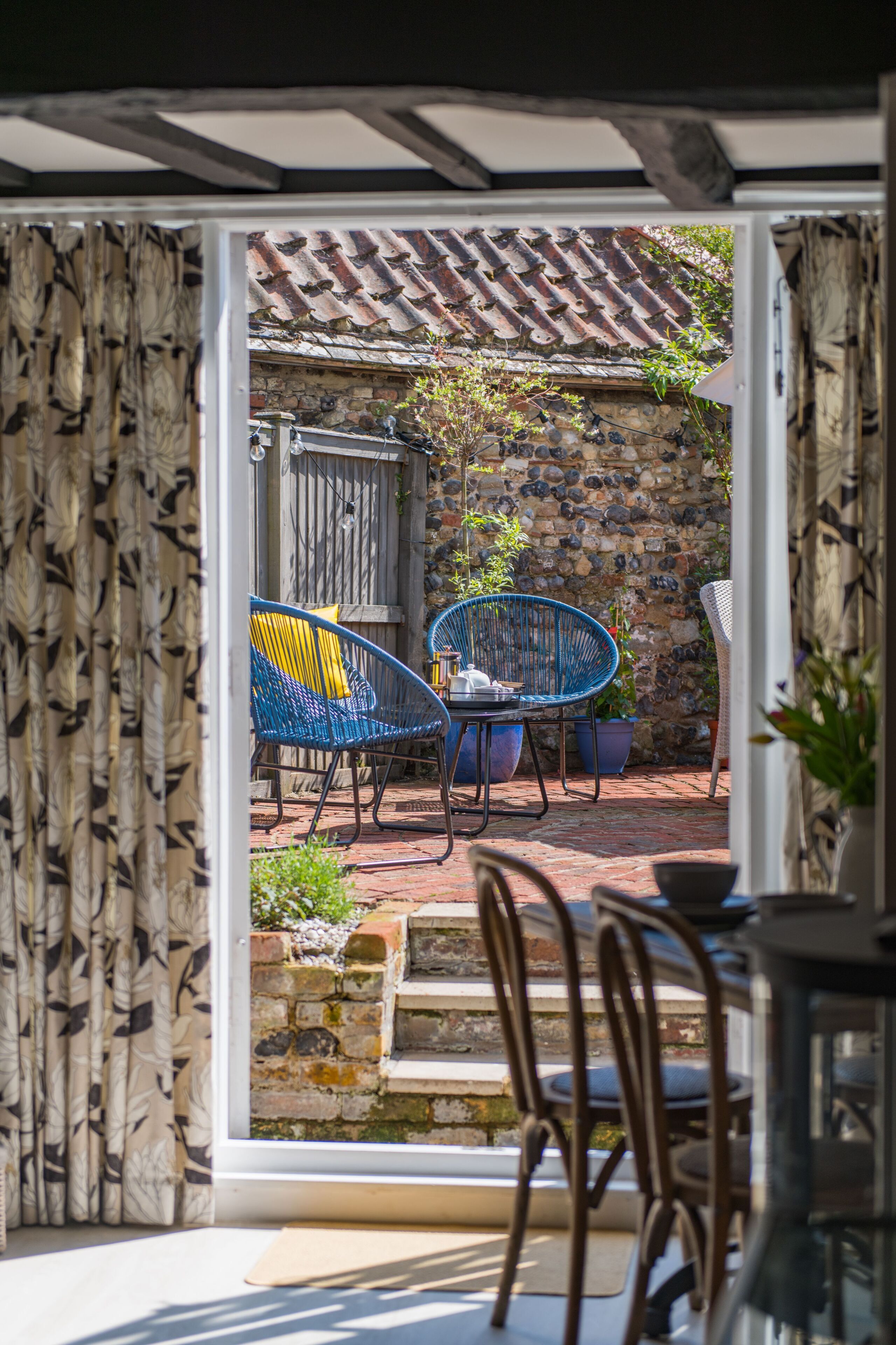 Une porte ouverte donne sur un patio agrémenté d’un mur en pierre, d’une clôture en bois et d’une table avec des chaises.