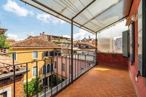 Un balcón con vista a edificios de tejas rojas, una barandilla metálica y un suelo de baldosas.
