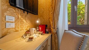 A room with a wooden table, a red coffee machine, a television mounted on the wall, and a view of greenery outside. - Ca' Beatrice (Venice)