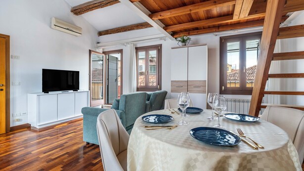 A dining area with a table set for two, a television in the background, and wooden beams on the ceiling. - Ca' Beatrice (Venice)