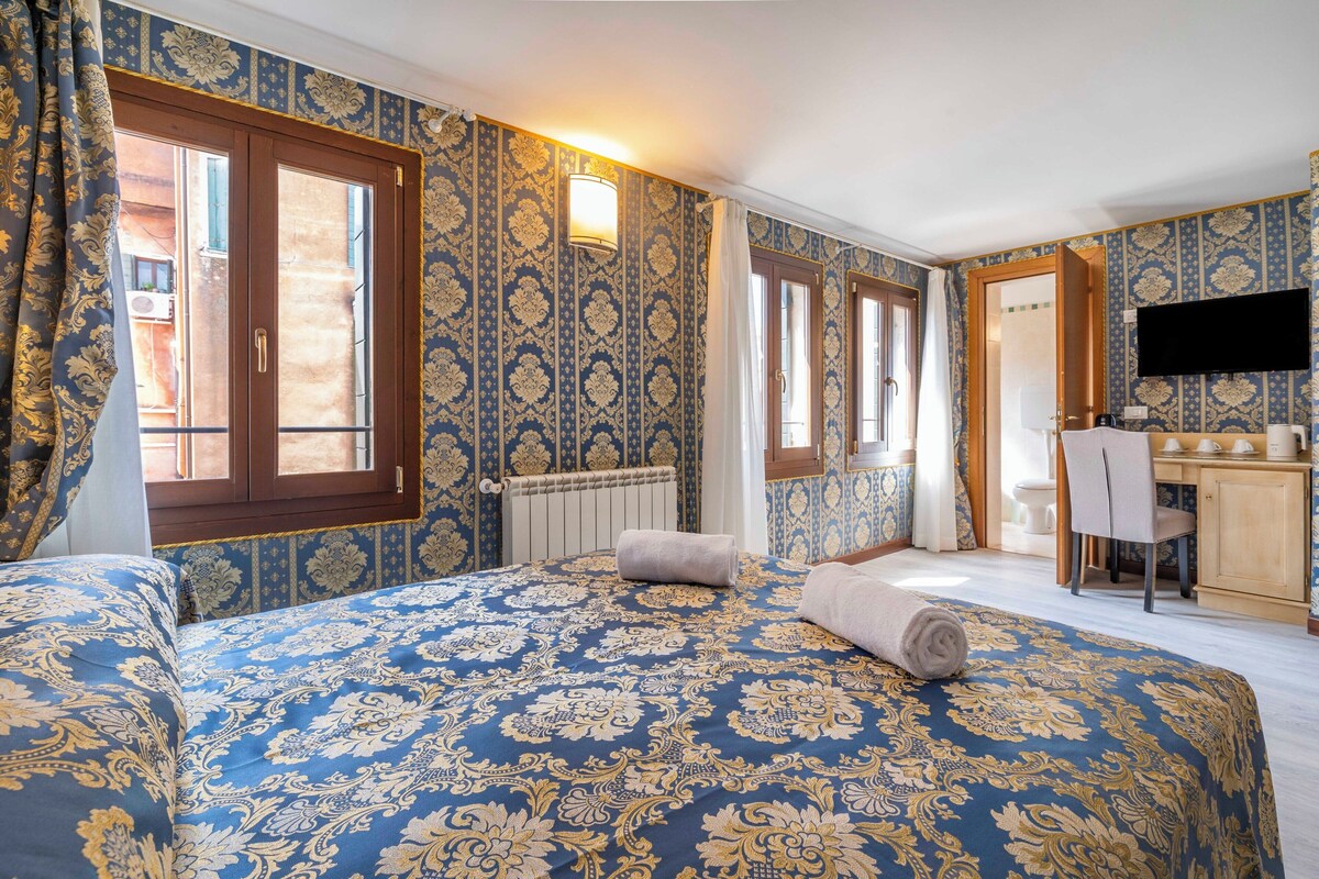 A hotel room with a large bed, a desk, a television, and a window with curtains.