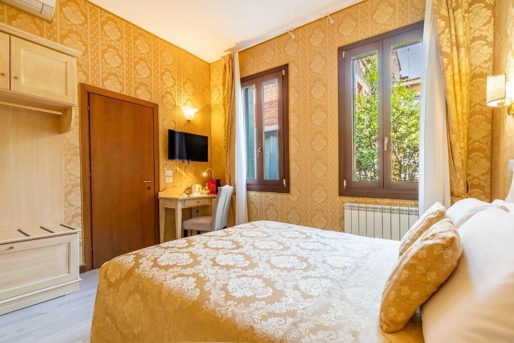 A hotel room with a bed, a desk, a television, and a window with curtains.