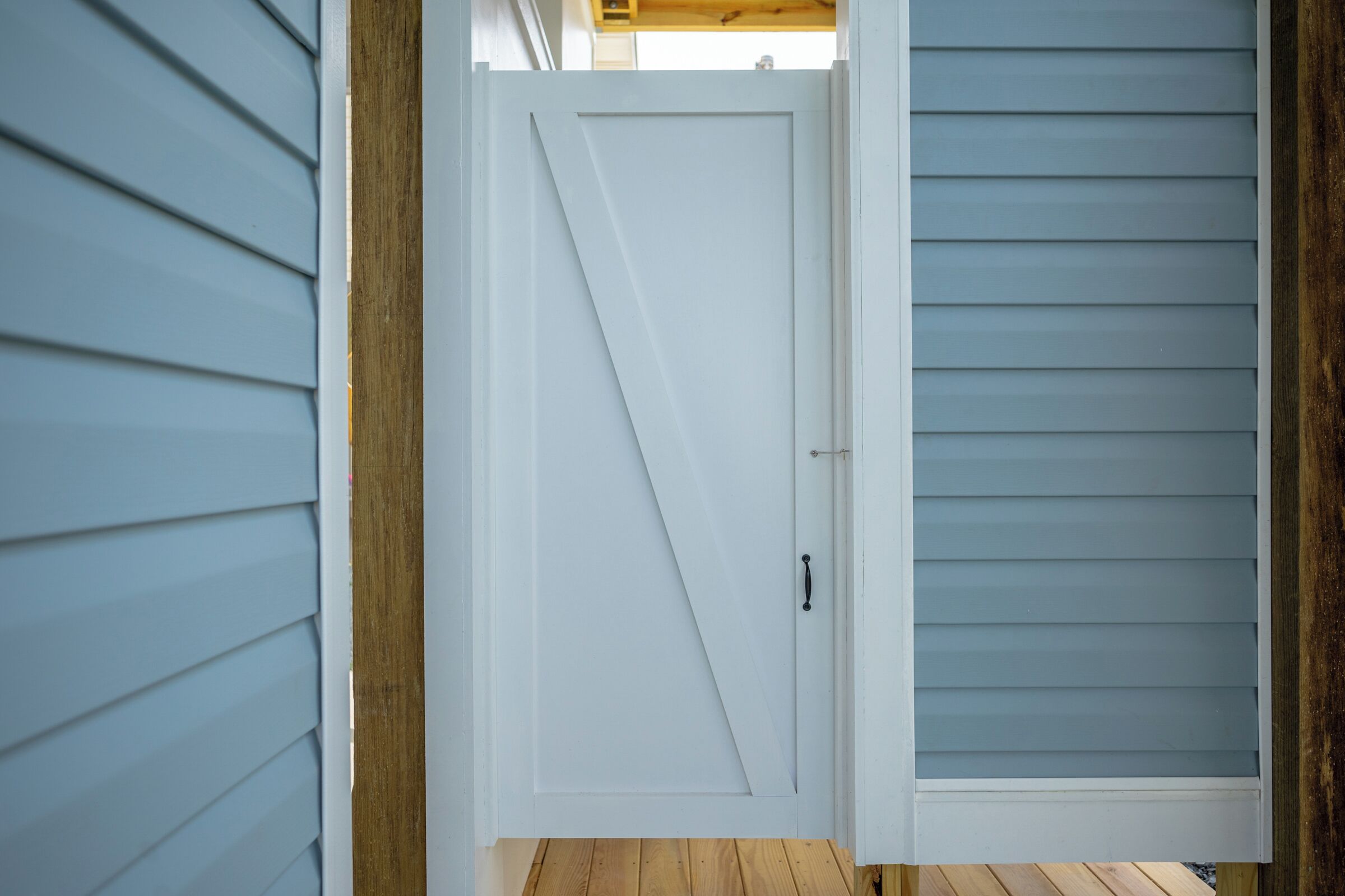 Una puerta blanca con un picaporte diagonal, enmarcada por molduras de madera y revestimiento azul claro.