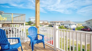 Un pontile in legno con due poltrone Adirondack blu, una ringhiera bianca e vista sulle case e sulla spiaggia.