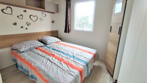 A bedroom with a bed, a window with curtains, a wall with heart decorations, and a wardrobe. - Mobil home 3 chambres (Saint-Jean-de-Monts)