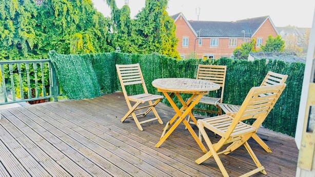 A wooden deck with a round table and four chairs, surrounded by a green hedge. - Hyperion in Newmarket (Newmarket)