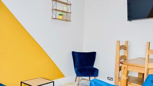 A room with a yellow and white wall, a blue chair, a wooden chair, a small table, and a TV mounted on the wall. - Hyperion in Newmarket (Newmarket)