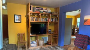 Een gezellige woonkamer met een houten boekenkast vol boeken, een flatscreen televisie, een kamerkleed met dessin en een klein houten tafeltje.
