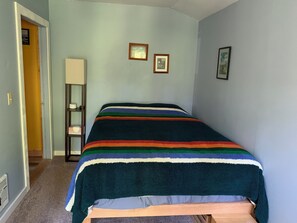 Una habitación con una cama, una mesita de noche, una lámpara y dos cuadros en la pared.