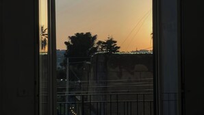 Une pièce avec une table et des chaises, une porte-fenêtre coulissante donnant sur un balcon extérieur d’où l’on peut admirer les arbres et les bâtiments.
