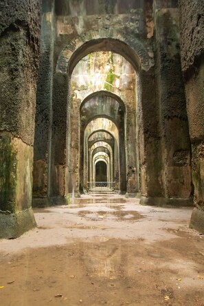 Un couloir bordé d’arches et de colonnes en pierre, qui mène à une arche située au loin.