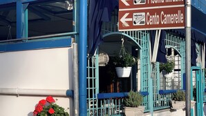 Un bâtiment à la façade bleue et blanche, une enseigne indiquant les directions vers « Piscina Mirabile » et « Cento Camerelle », et un pot de fleurs orné de fleurs rouges.