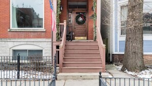 A two-story house with a front porch, a front door with a wreath, and a flag.
