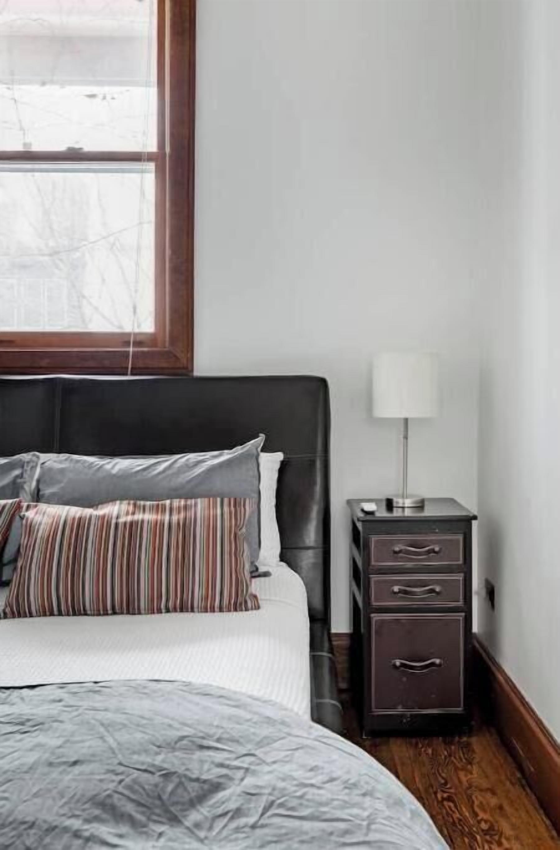 A bedroom with a bed, a nightstand, and a window.