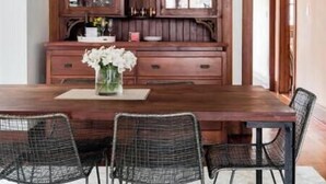 A dining area with a wooden table, wire mesh chairs, and a cabinet with glass doors.