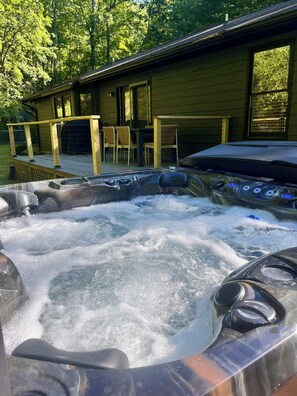 Ein Whirlpool mit Holzterrasse und Stühlen, umgeben von Bäumen.