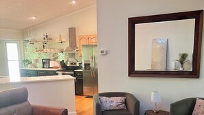 Una sala de estar moderna con un sofá de cuero marrón, una mesa de centro oscura y dos sillones. Un espejo grande cuelga en la pared, reflejando la habitación.