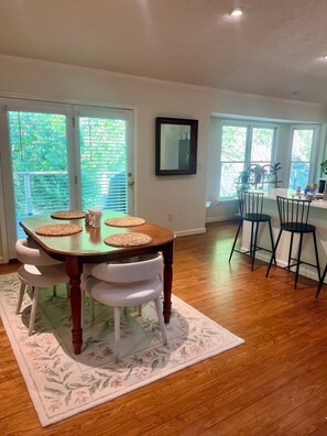 Un comedor con una mesa de madera, sillas blancas y un tapete floral.