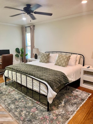 Un dormitorio con cama, escritorio, silla, ventilador de techo y ventana con cortinas.