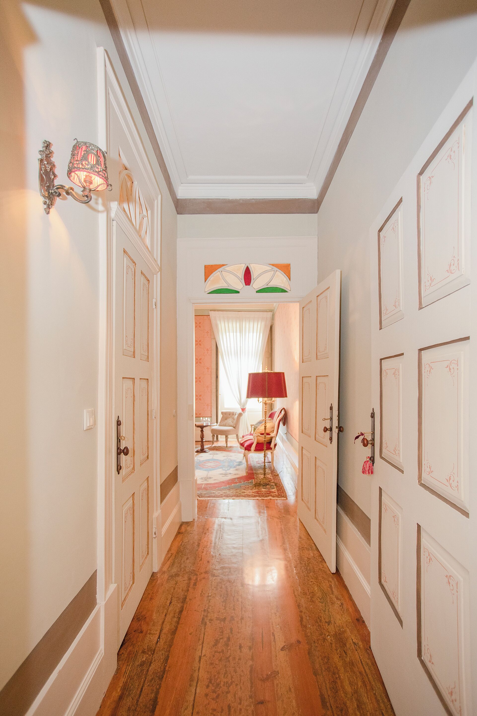 A hallway with wooden flooring, white doors, and a chandelier.