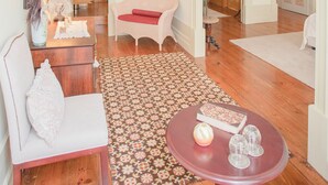 Un salon spacieux avec un plancher en bois, un tapis à motifs, une table rouge et un canapé blanc.