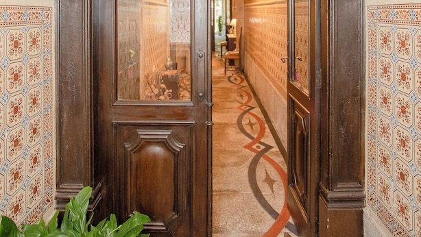 Un couloir avec une porte en bois, des murs à motifs et un tapis orné d’un dessin géométrique.