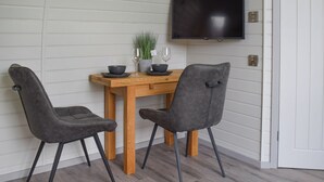 A dining area with a wooden table, two grey upholstered chairs, a potted plant, and a flat-screen TV mounted on the wall. - Laurel Pod - UK47203 (Lathom, near Southport)