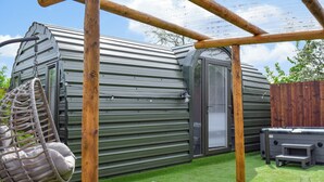 A metal structure with a hanging chair, a grill, and a cushioned seating area. - Laurel Pod - UK47203 (Lathom, near Southport)