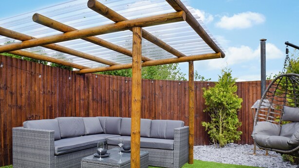 A covered outdoor seating area with a wooden pergola, a grey sectional sofa, and a hanging chair. - Laurel Pod - UK47203 (Lathom, near Southport)