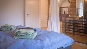 Una cama bien hecha con toallas dobladas, una puerta blanca y vistas a un muro de ladrillo y un balcón.