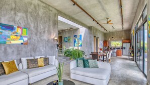 A spacious living area with a modern sofa set, a coffee table, and a dining area with a kitchen in the background.