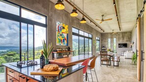 A modern kitchen with a large island, dining area, and a view of the landscape.