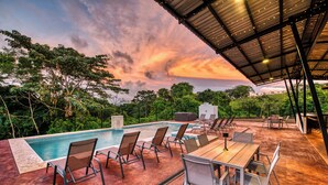 A poolside area with a covered seating area, lounge chairs, and a hot tub.