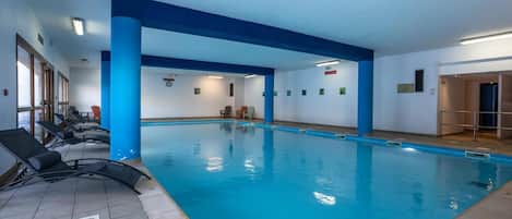 An indoor swimming pool with blue pillars, lounge chairs, and a tiled floor.