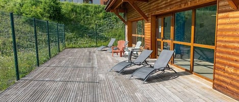 A wooden deck with lounge chairs and a glass-enclosed room.
