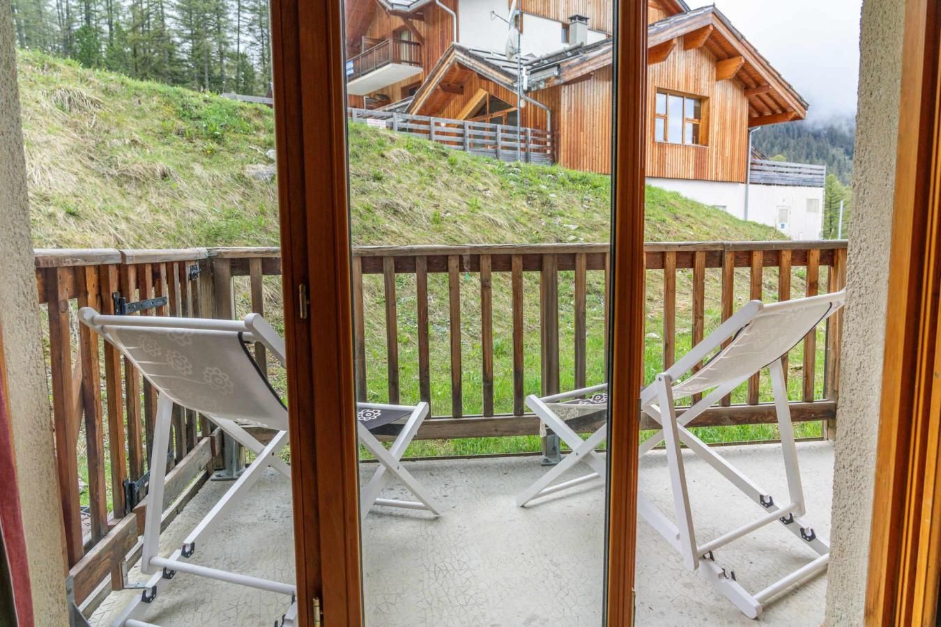 A balcony with two white lounge chairs and a wooden railing.