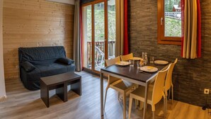 A cozy living room with a dark grey sofa, a wooden coffee table, and a dining area with a dark table and white chairs. - 200m from resort center, 3rd floor, swimming pool, tv, ski locker, 23m², Les Orres (Les Orres)