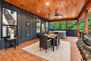 Un espacio exterior techado con terraza de madera, mesa de comedor con sillas, jacuzzi y parrilla.