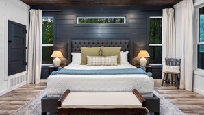 A bedroom with a dark wood headboard, a large bed with white bedding, two bedside lamps, and a bench at the foot of the bed. - Family Retreat | Perfect Location | Hot Tub (Broken Bow)