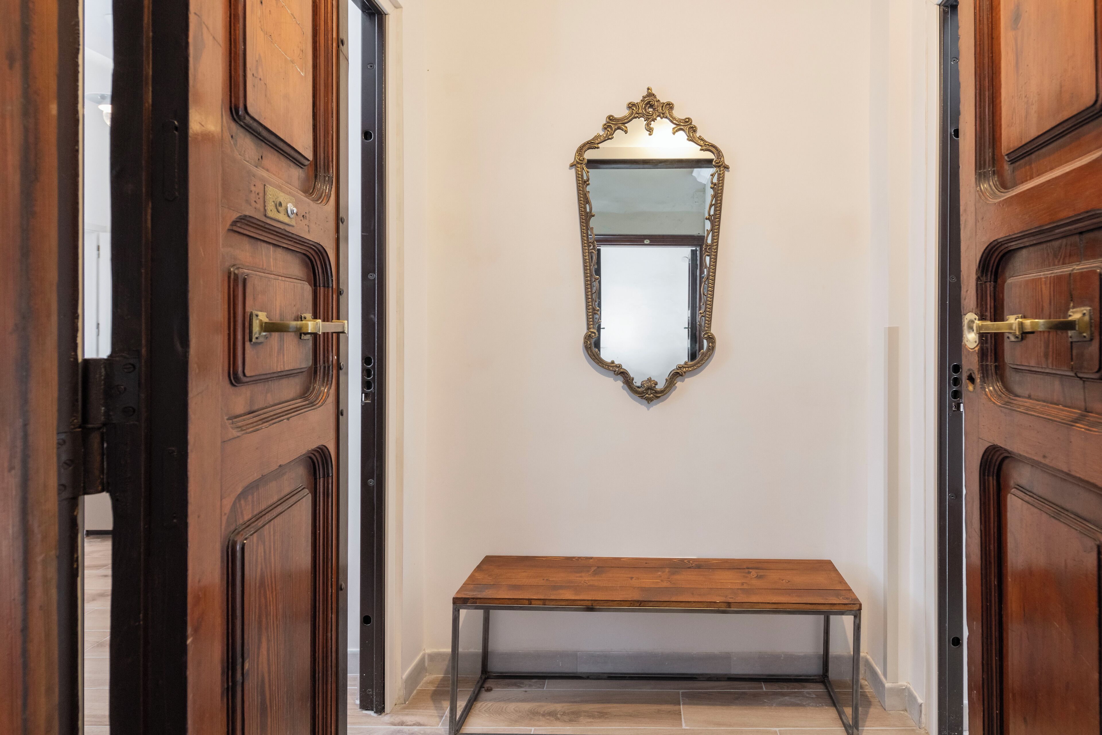 A hallway with wooden doors, a bench, and a mirror on the wall.