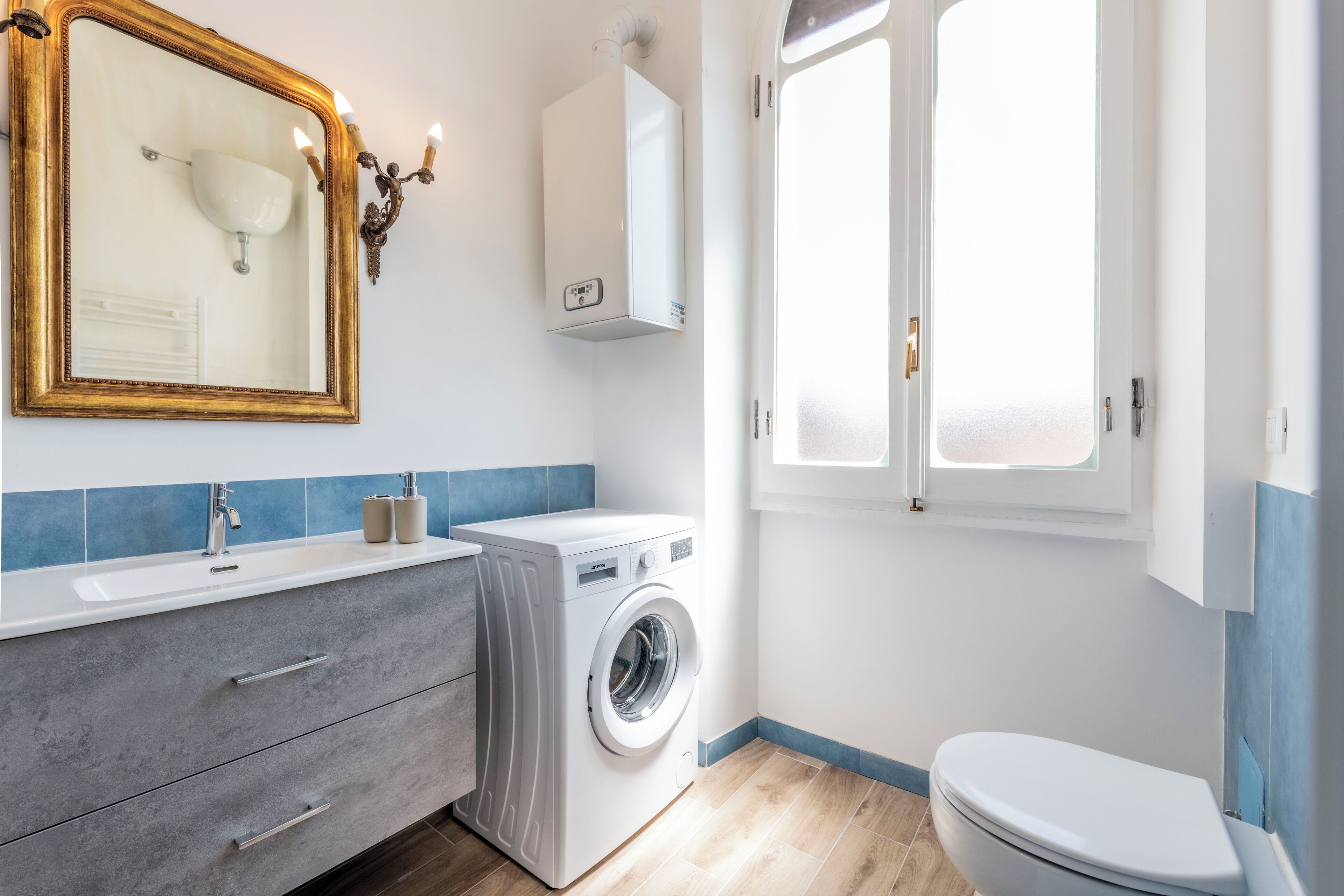A bathroom with a washing machine, a sink with a mirror, and a toilet.