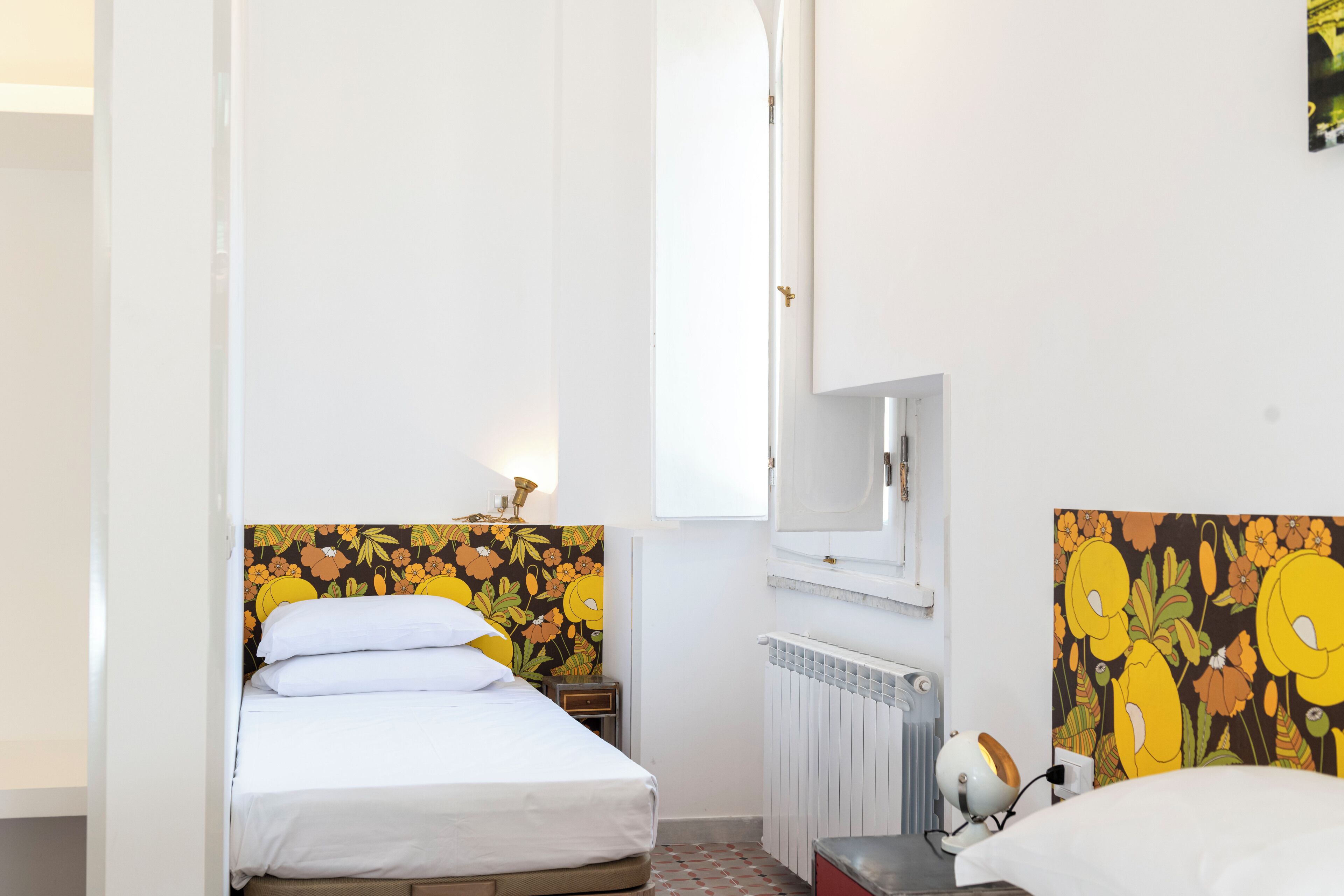 A small, clean room with a bed, a nightstand, a radiator, and a mirror.