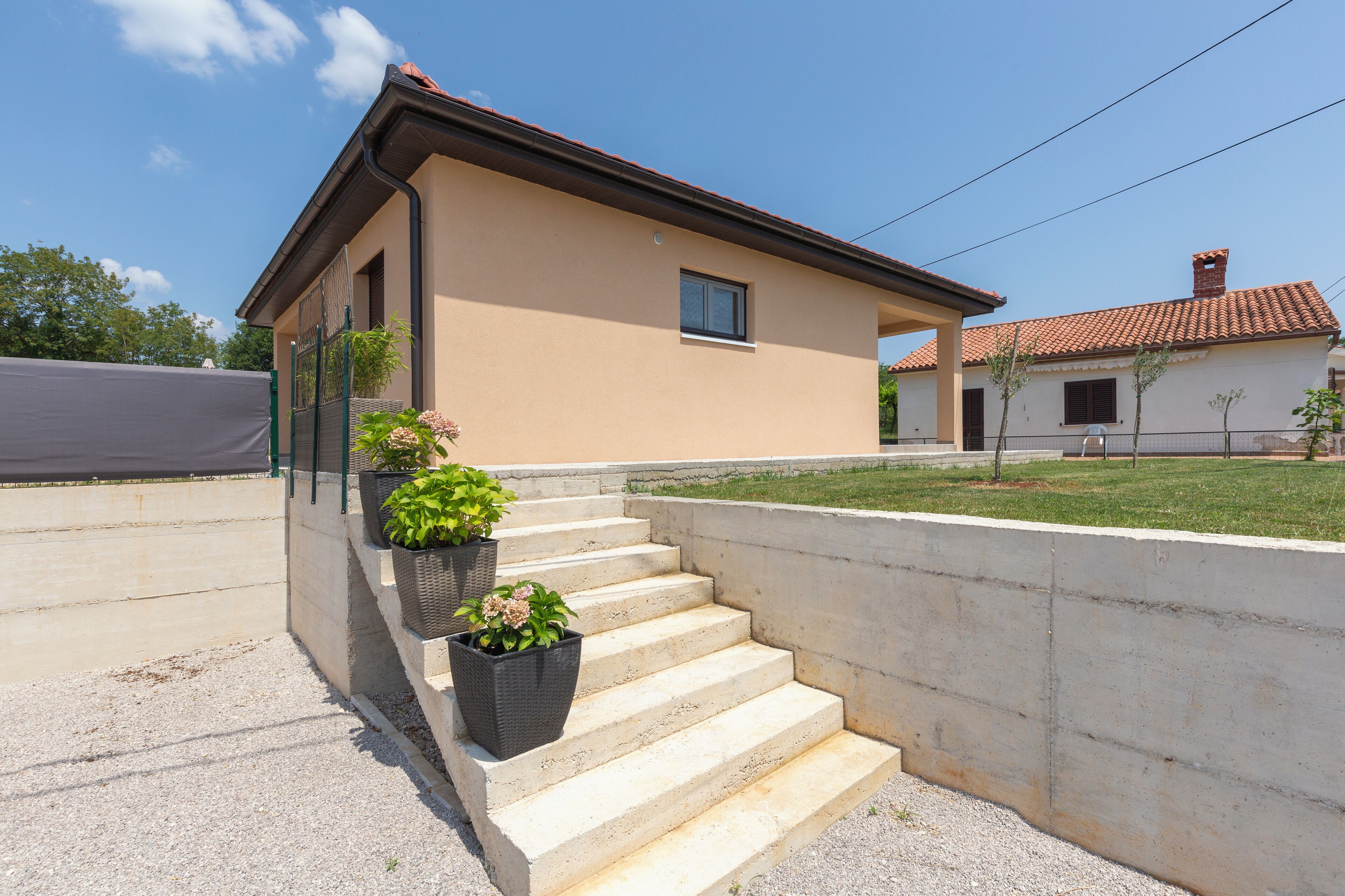 Ein zweistöckiges Haus mit sandfarbenem Anstrich, einem roten Ziegeldach und einer Betonsteintreppe, die zum Eingang führt.