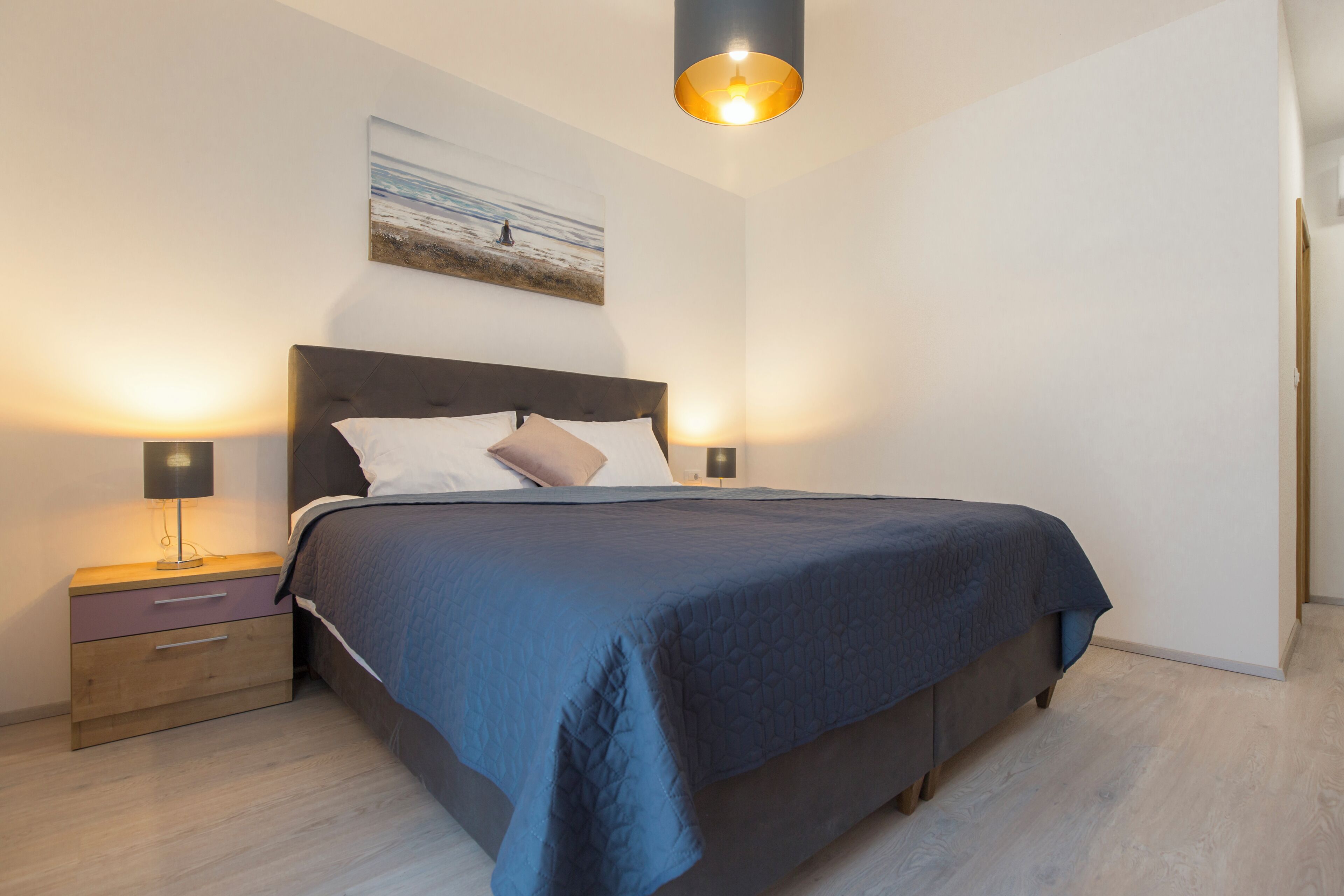 Un dormitorio moderno con una cama grande, dos mesitas de noche, una lámpara de pared y un cuadro sobre la cama.