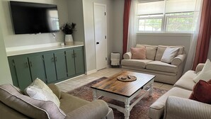 Ein Wohnzimmer mit einer Couch, einem Couchtisch und einem an der Wand montierten Fernseher.
