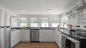 A modern kitchen with white cabinets, stainless steel appliances, and a wooden floor.