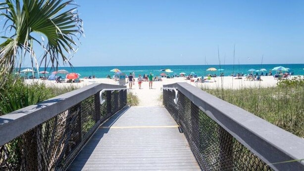 A wooden boardwalk leading to a beach with umbrellas and people.