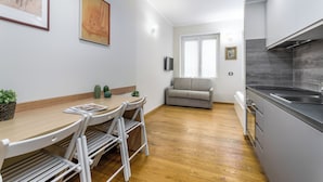 A modern kitchen with a wooden dining table, white chairs, and a grey sofa in the background. - Casa da Suite Cadorna (Milan)