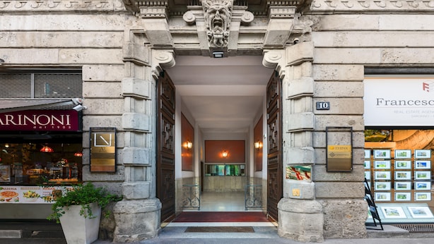 A stone building entrance with a potted plant, a restaurant sign, and a real estate agency sign. - Casa da Suite Cadorna (Milan)