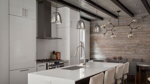 Una cocina moderna con armarios blancos, una isla central con taburetes de bar, una campana extractora de acero inoxidable y una pared de madera.